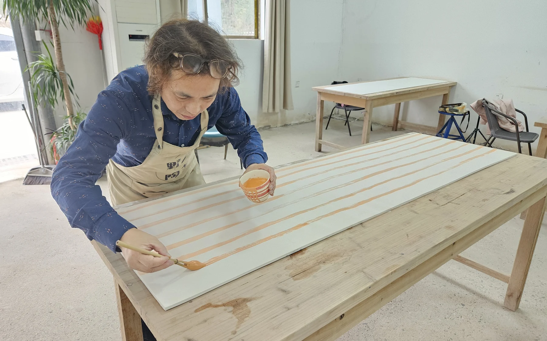 YE Xingqian paints a long porcelain panel in the studio